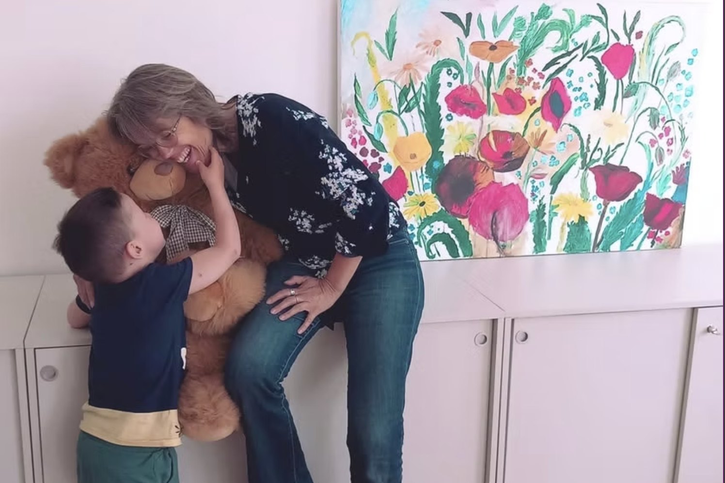 Judith buigt zich voorover om een jongen te knuffelen die een grote teddybeer vasthoudt