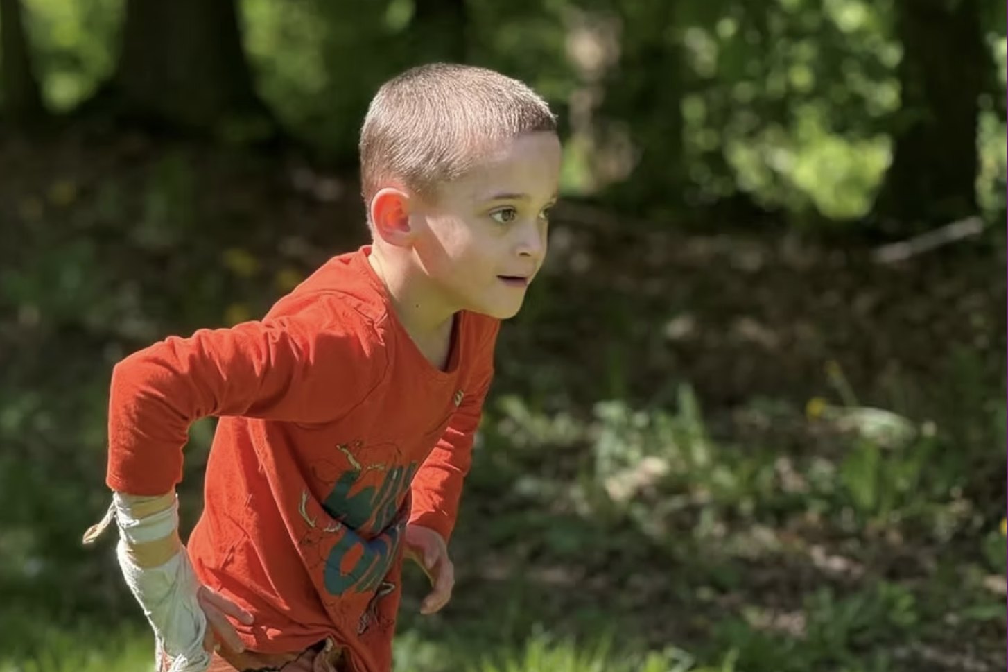 Een jongen in een oranje shirt loopt door zonnig gras